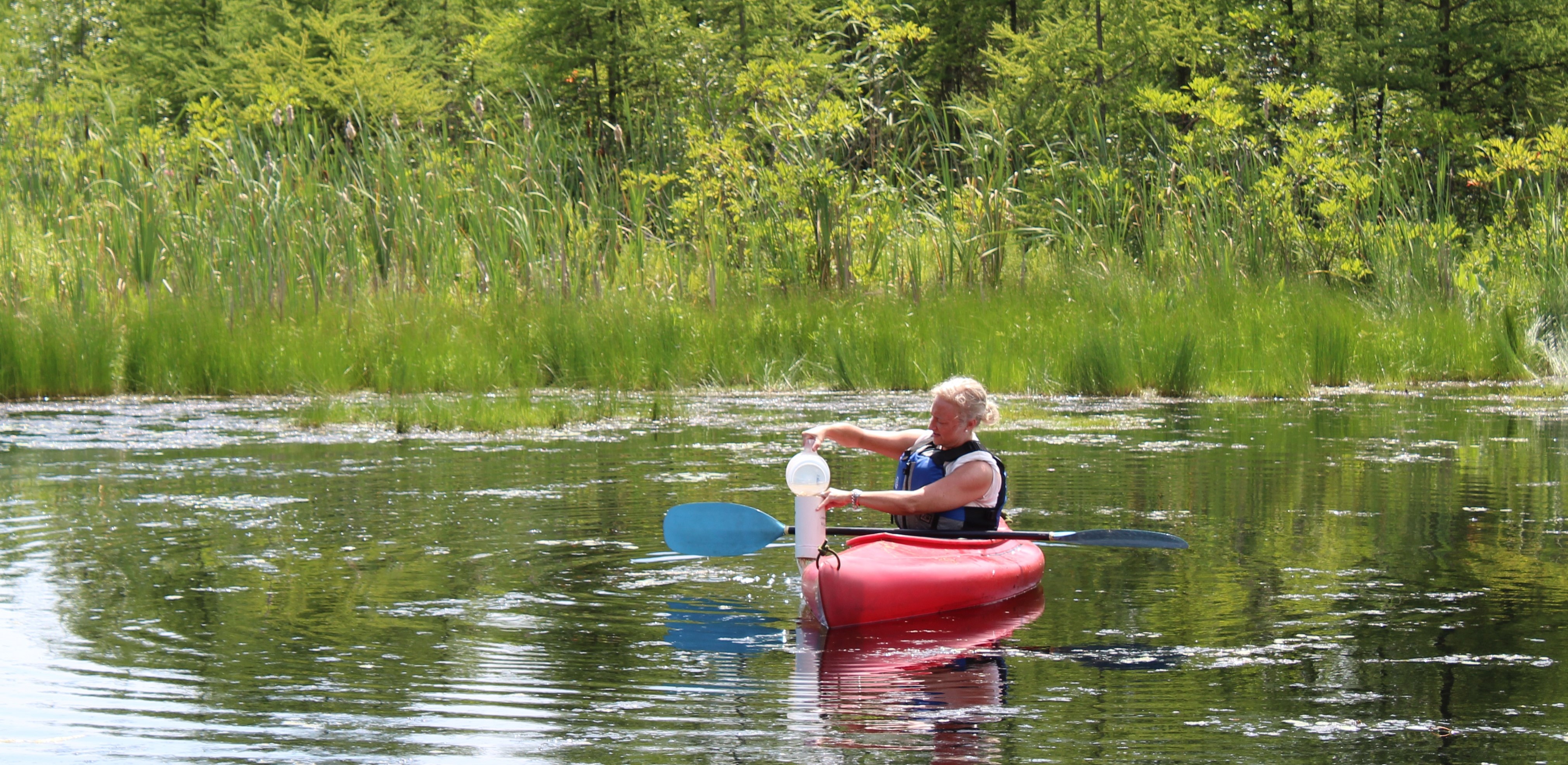 "Pam on a lake in a kayak taking a water sample"
