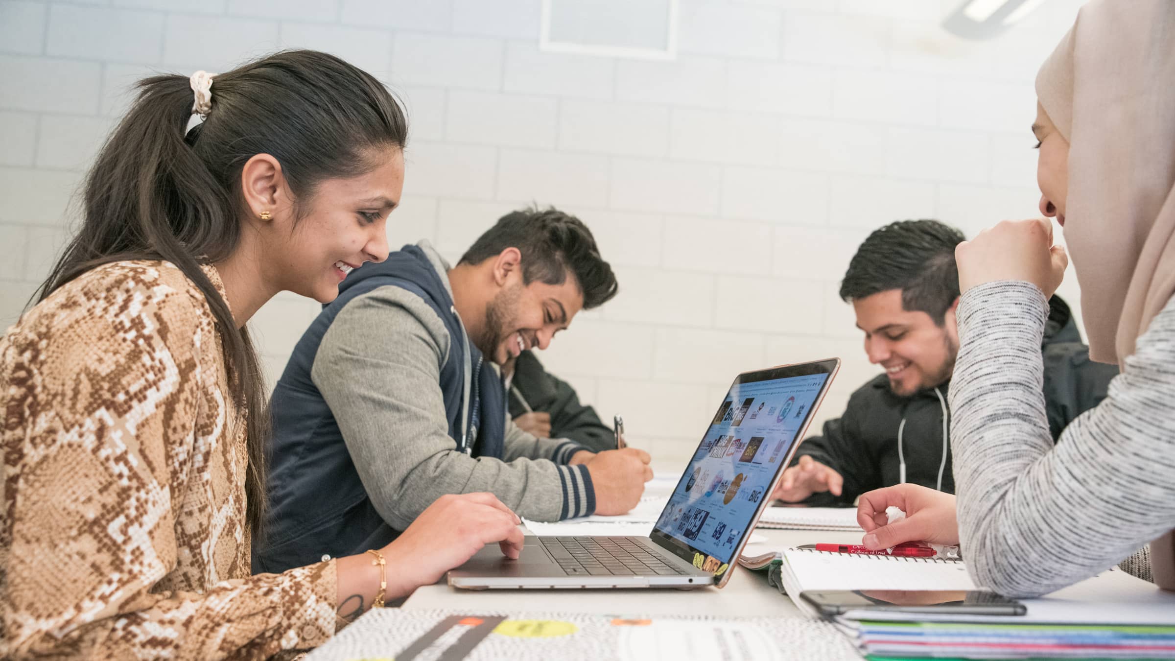 A group of two male and two female students sit around a table with laptops and notebooks to work on a project at NEIU's College of Business and Technology
