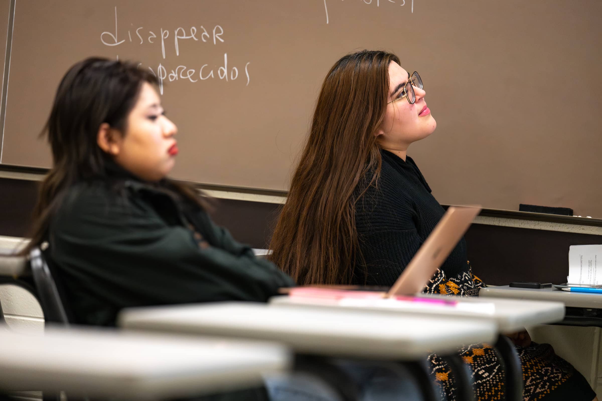 Two female students sit at desks in a classroom