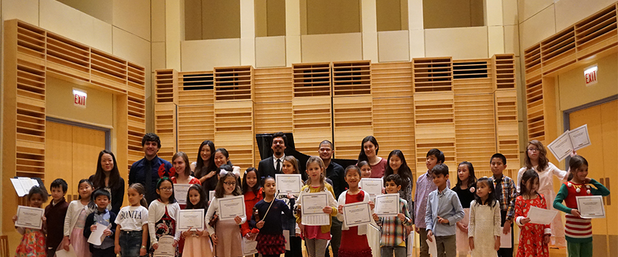 People stand on the Recital Hall stage for a community music recital.