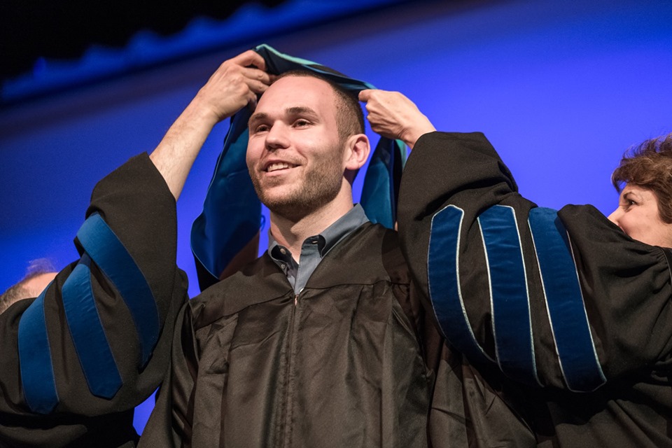 Two people drape a hood over a male graduate's head at the Master's Hooding Ceremony