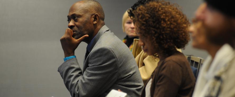 A black man in a gray suit listens intently at the 2nd Annual Genocide Research Symposium