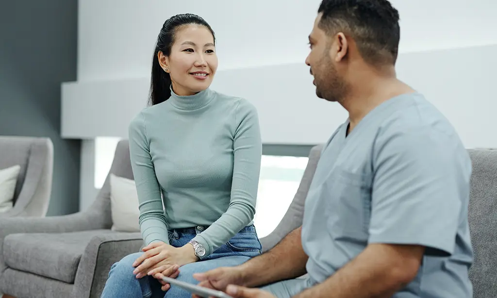 A man and a woman sitting on chairs in a hospital having a conversation