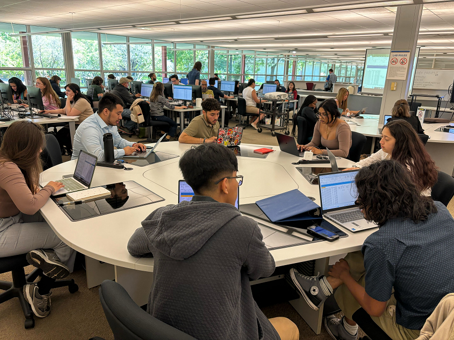 Group of Students Sitting Around A Table With Laptops Working An Excel project.