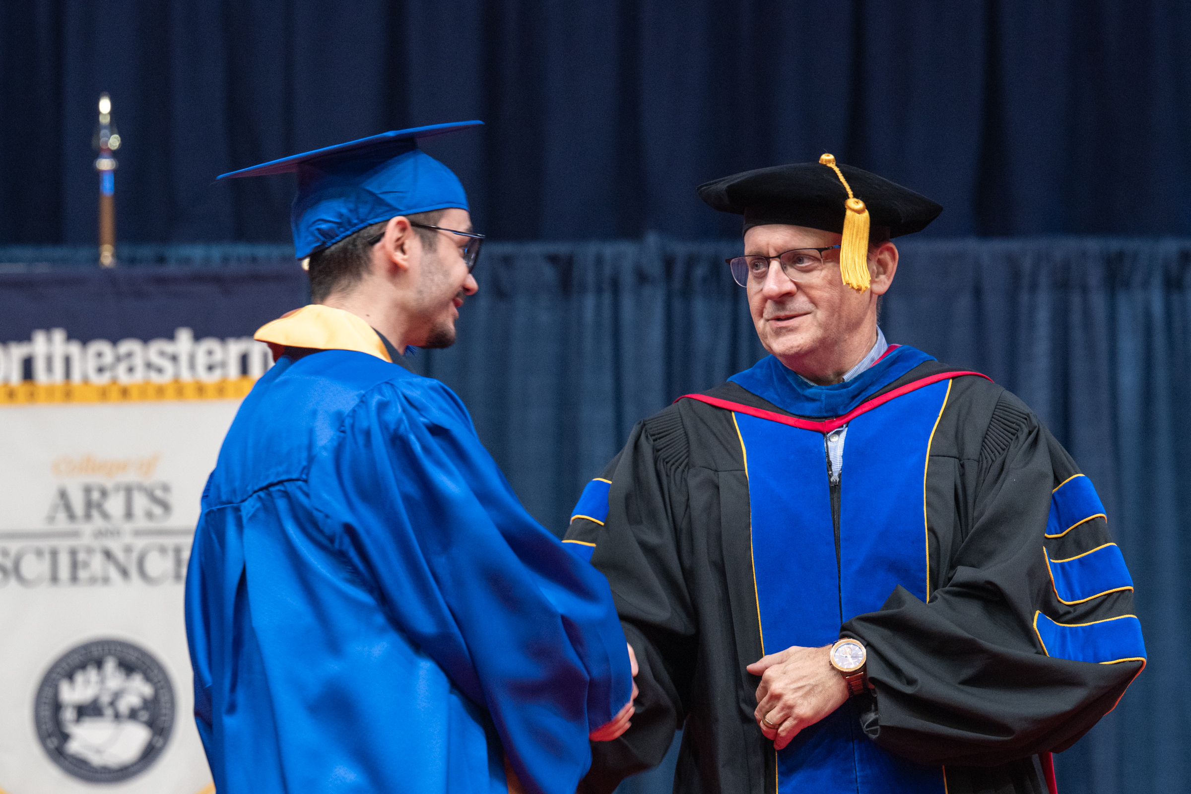 Dr Michael Bedell shakes a student's hand on stage at the Spring 2025 Commencement ceremony.