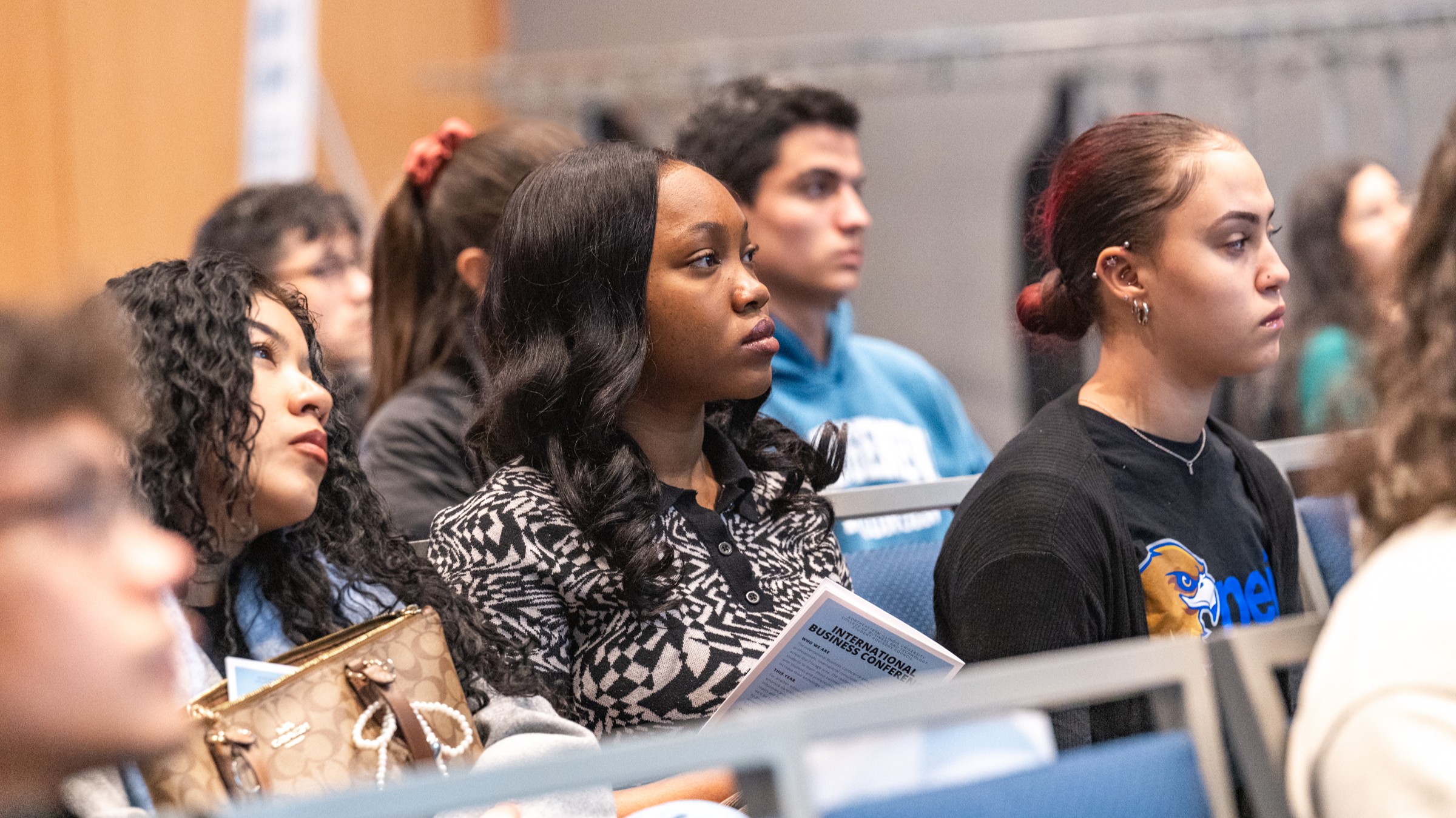 Students seated at a conference, looking up at the stage 