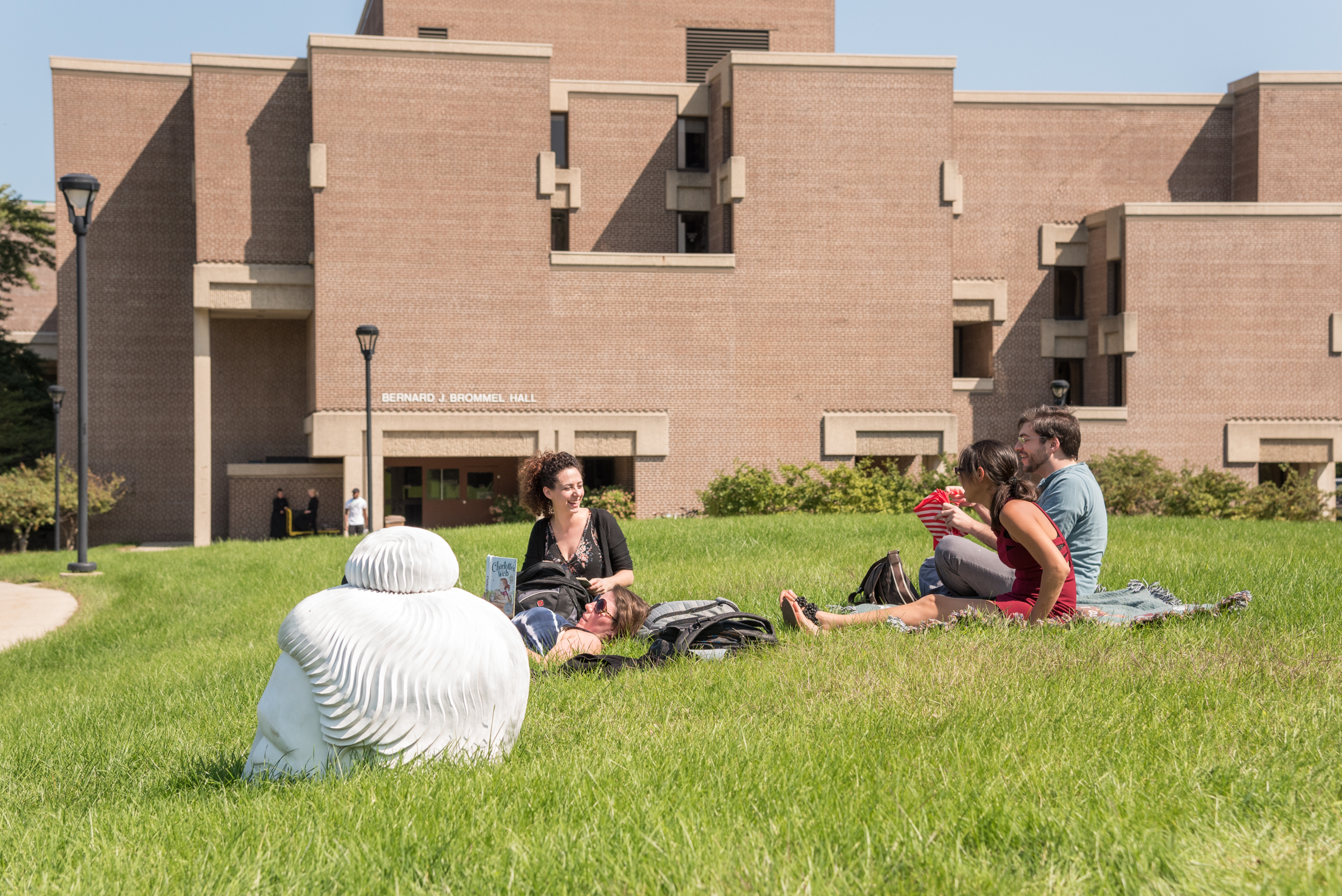 Students sitting on open lawn with science building in the background. 
