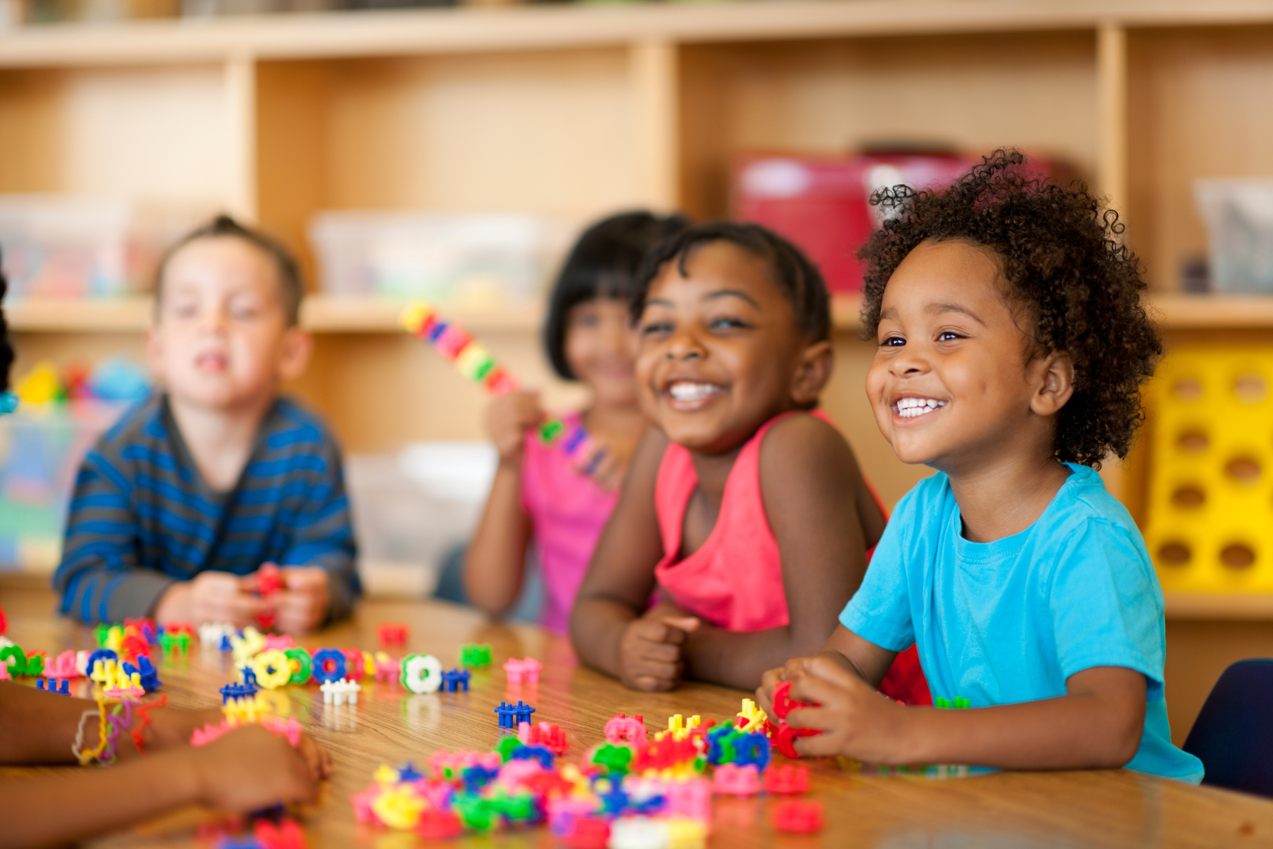 A few young children sitting around a table with toys on top. 