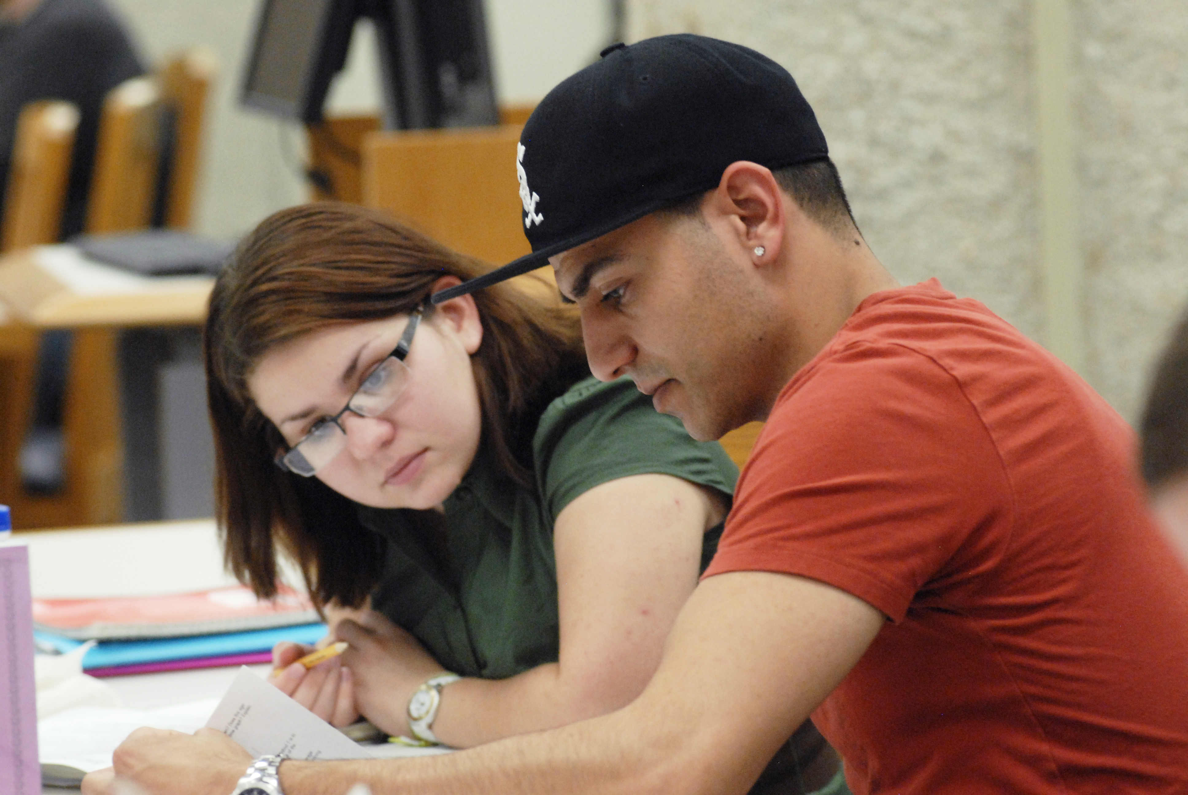 Male and female student sitting at a table, examining a paper. 
