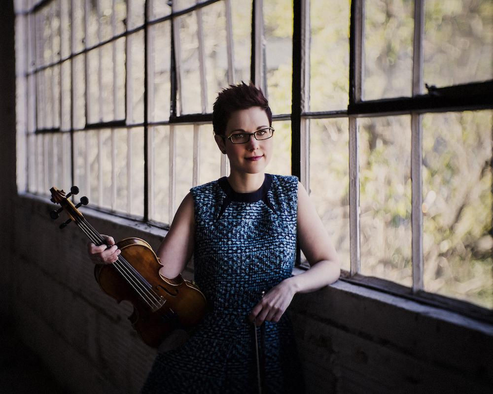 April Verch holding a violin and standing in front of a window