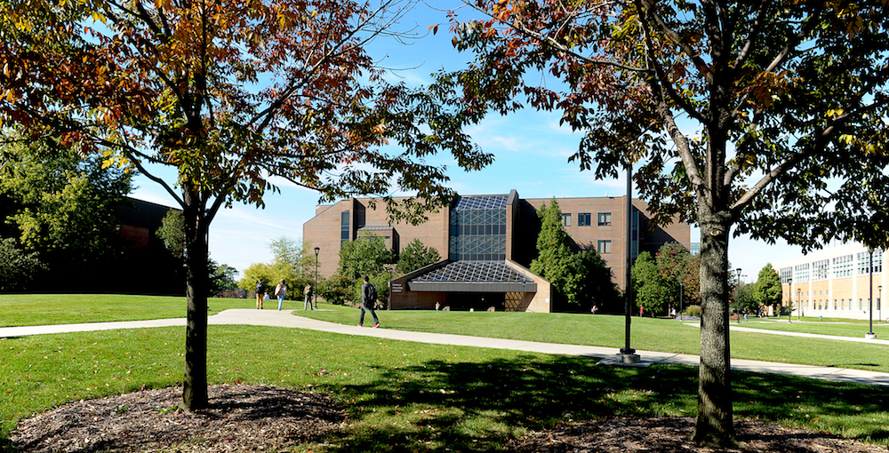 The Ronald Williams Library exterior with two trees in the foreground and students walking the paths of the University Commons