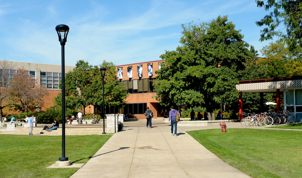Partial view of the south side of the Fine Arts Building, Student Union and B Building with students walking and relaxing