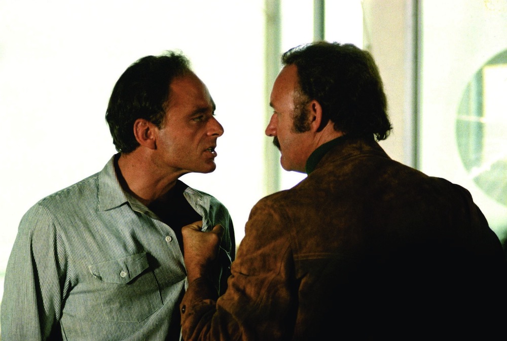 A still image from the film "Night Moves," in which two men face each other while the man on the right grabs the shirt of the man on the left.