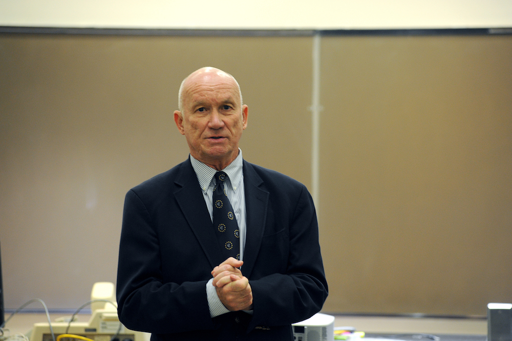Economics Professor Emeritus Edward Stuart speaks at the front of a classroom.
