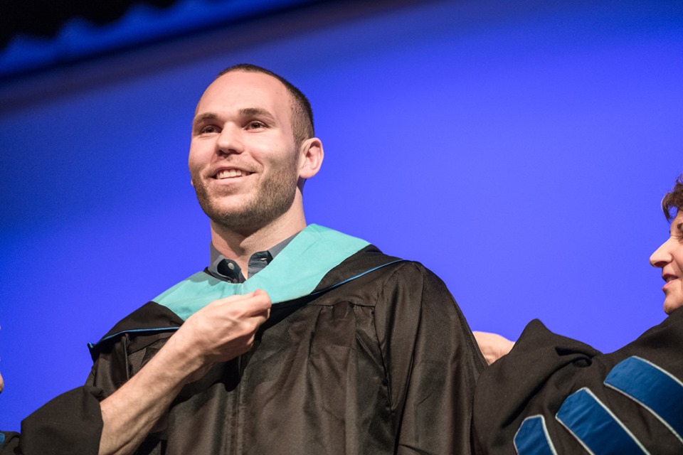 Two people drape a hood over a male graduate's head at the Master's Hooding Ceremony