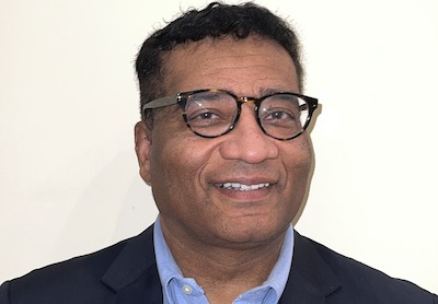 Photo of Christopher Childers wearing black rimmed eye glasses, a blue shirt and dark blazer against a white background 