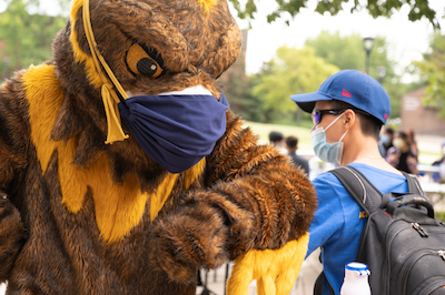 A masked Goldie bumps elbows with a masked student