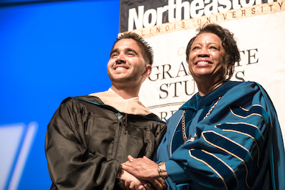 President Gibson and a student wear regalia as they stand side by side