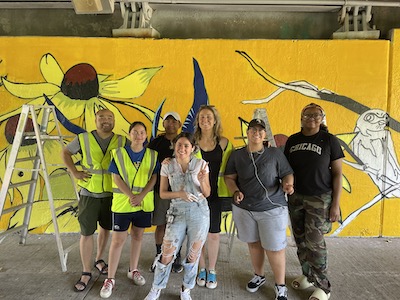 Students stand in front of a mural featuring birds and native plants