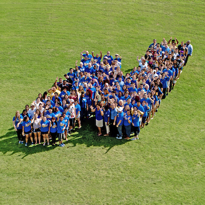 A large group of people stand together outside to form NEIU's Flying N logo