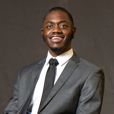 Javonti Mordican wearing a gray suit, white shirt, black tie and smiling