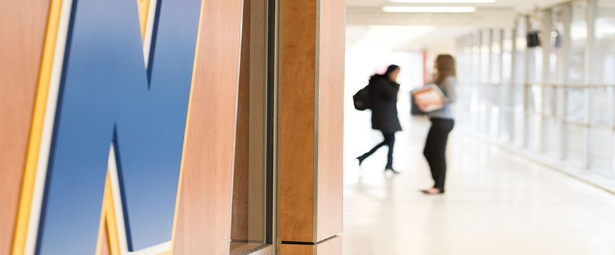 Students walk past the NEIU logo on the wall.