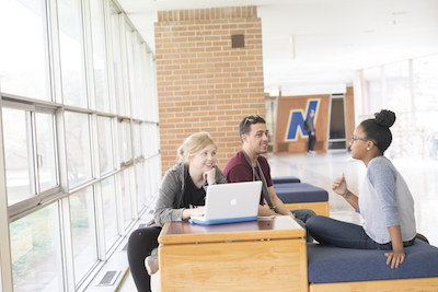 Three students sit near the NEIU Admissions office working on a laptop