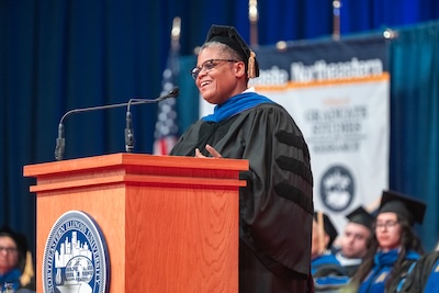 A photo of Keeanga-Yamahtta Taylor, Ph.D., wearing black graduation regalia, speaking at the Commencement podium.