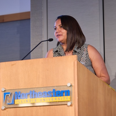 A photo of Jennifer Franco, speaking at a podium, accepting her Alumni Award.