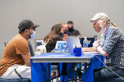 Photo of a student in a face mask sitting at a table meeting an academic advisor at NEIU's Fall registration event on June 28, 2021