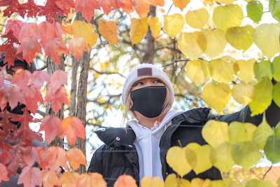 A student wearing a face mask surrounded by tree leaves