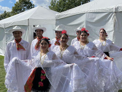 Eight dancers dressed in white costumes pose together outdoors