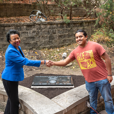 Photo of President Gloria J. Gibson in a blue blazer and U.S. veteran Gabriel Can (current student) unveiling a plaque dedicated to the U.S. Armed Forces.