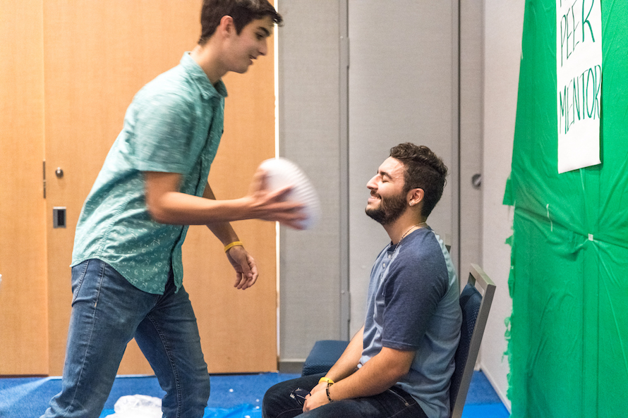 An FYE Peer Mentor sits smiling with eyes closed as a student pies him in the face