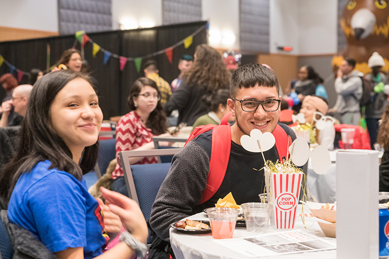 Students sit at a decorated table and smile together.