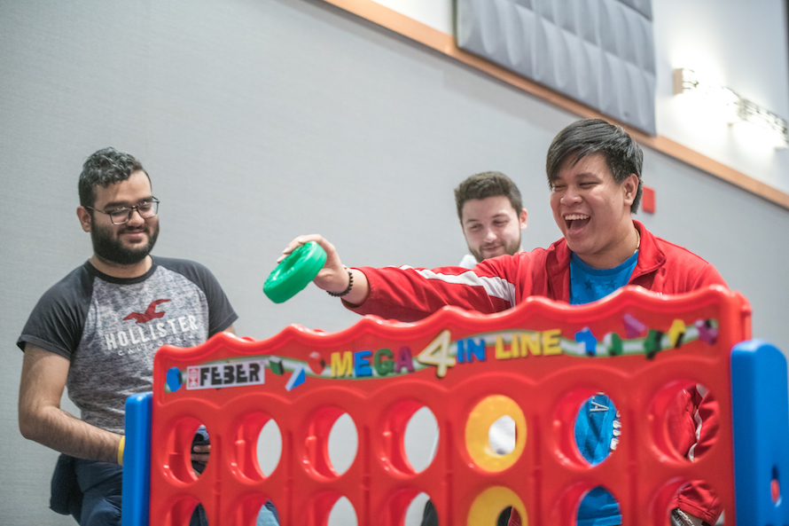 Student playing giant connect 4 holds smiles widely as he places green disk