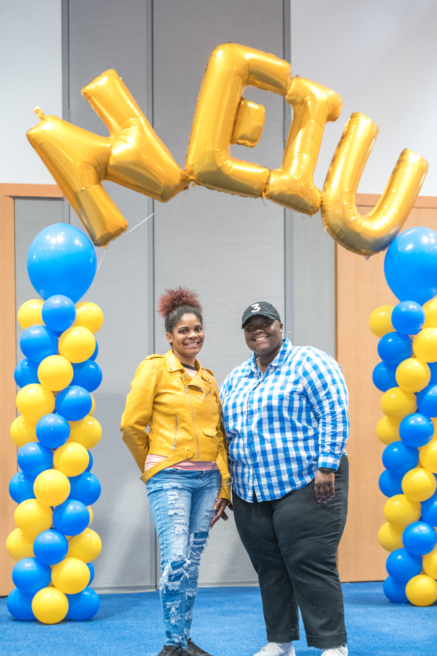 Two students pose below NEIU balloon marquee