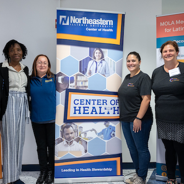 A group photo of Northeastern ChicagoCHEC collaborators in front of a banner with the text "Northeastern Illinois University Center of Health."