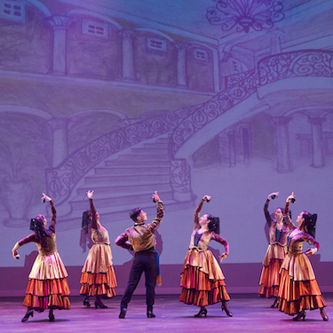 Six dancers in costume on stage raise their arms in unison