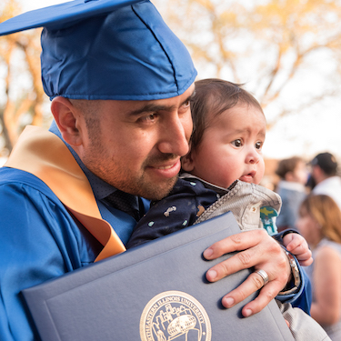 A photo of a Northeastern graduate holding their diploma cover and a child