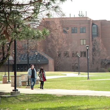 Photo of two people wearing face masks walking on the Main Campus with the Ronald Williams Library in the background