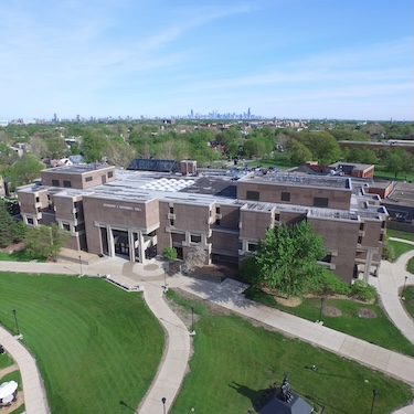 An aerial photo of Northeastern Illinois University's Main Campus with Bernard J. Brommel Hall in the foreground and the Chicago skyline in the background.