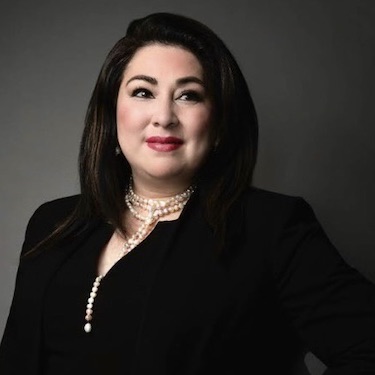 A headshot photo of Olga Camargo wearing black business attire and a white pearl necklace.