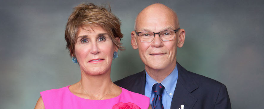 James Carville and Mary Matalin smile into the camera while standing in front of a gray background.