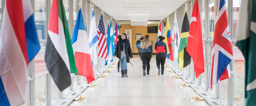 People walk past the flags of many nations line the glass hallway near the B Building