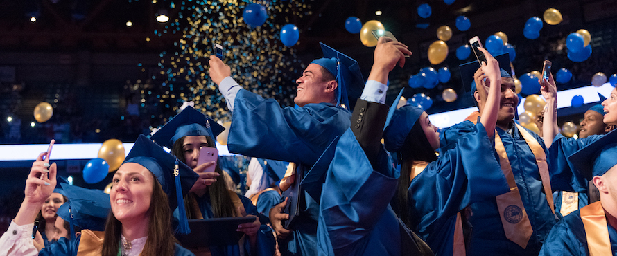 Blue and gold balloons and confetti shower graduates who are wearing regalia 