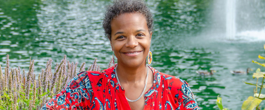 A photo of Durene I. Wheeler in a red top with blue flowers smiling, facing the camera. Water is in the background. 