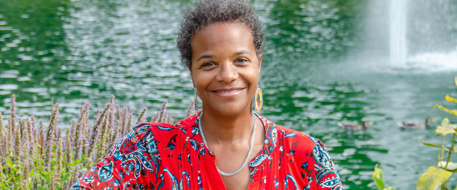 A photo of Durene I. Wheeler in a red top with blue flowers smiling, facing the camera. Water is in the background.