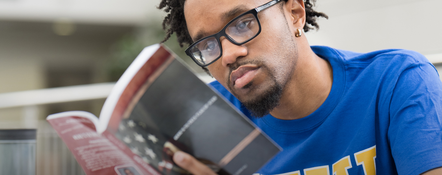 A Northeastern student wearing glasses and a blue t-shirt and reading a book
