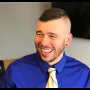 G. "Max" Maxin IV laughs while wearing a blue shirt and yellow tie.